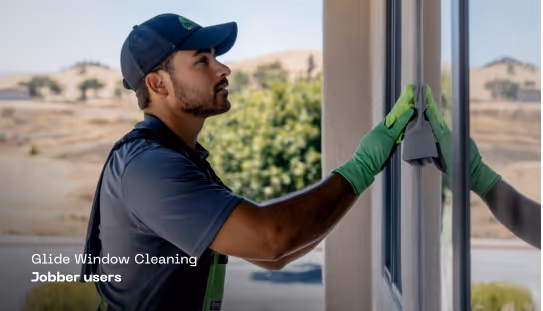 Man wearing green gloves cleaning a large window with a squeegee outdoors.