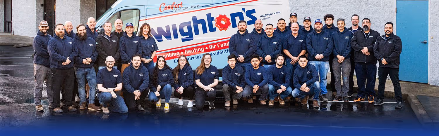 Group photo of a company team in navy uniforms posing in front of a van with Wighton's plumbing, heating, and air conditioning branding.