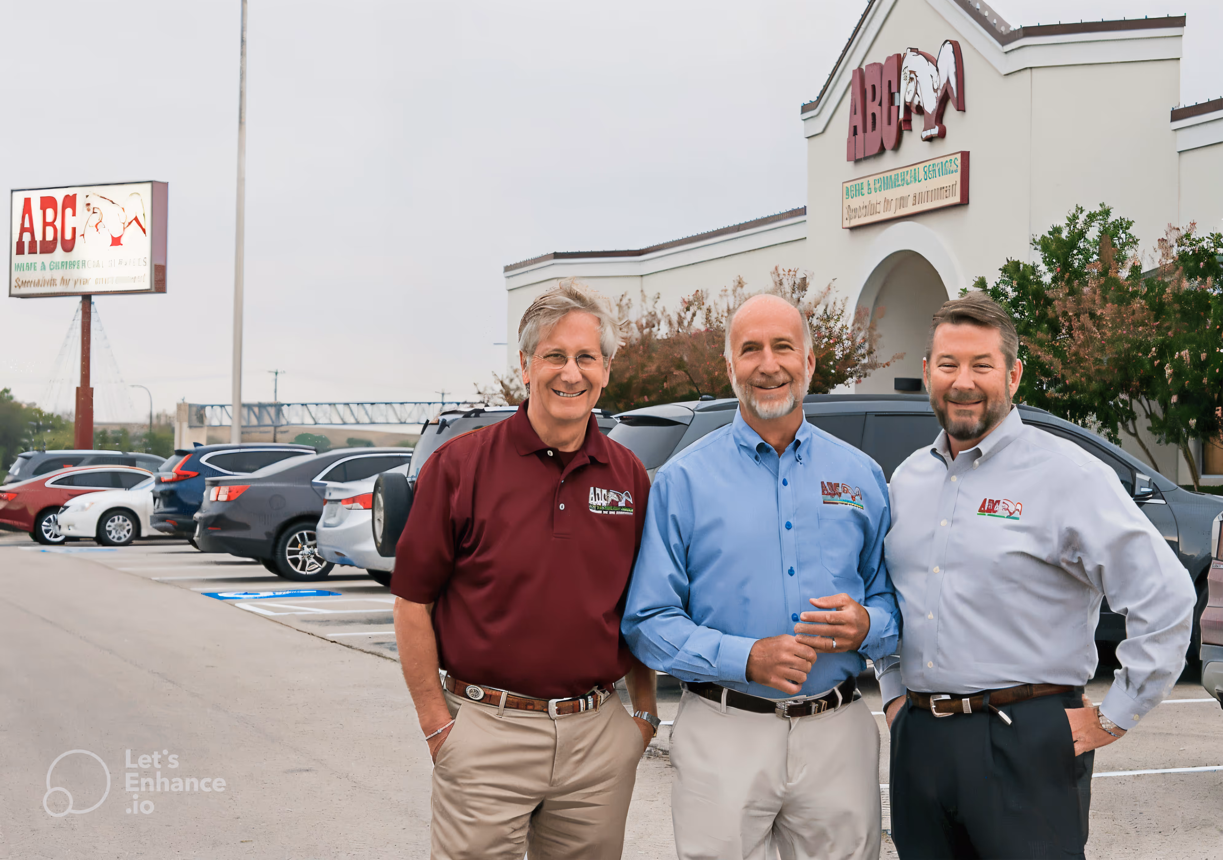 Three men wearing ABC company shirts standing and smiling in front of an ABC Home & Commercial Services building and parking lot.