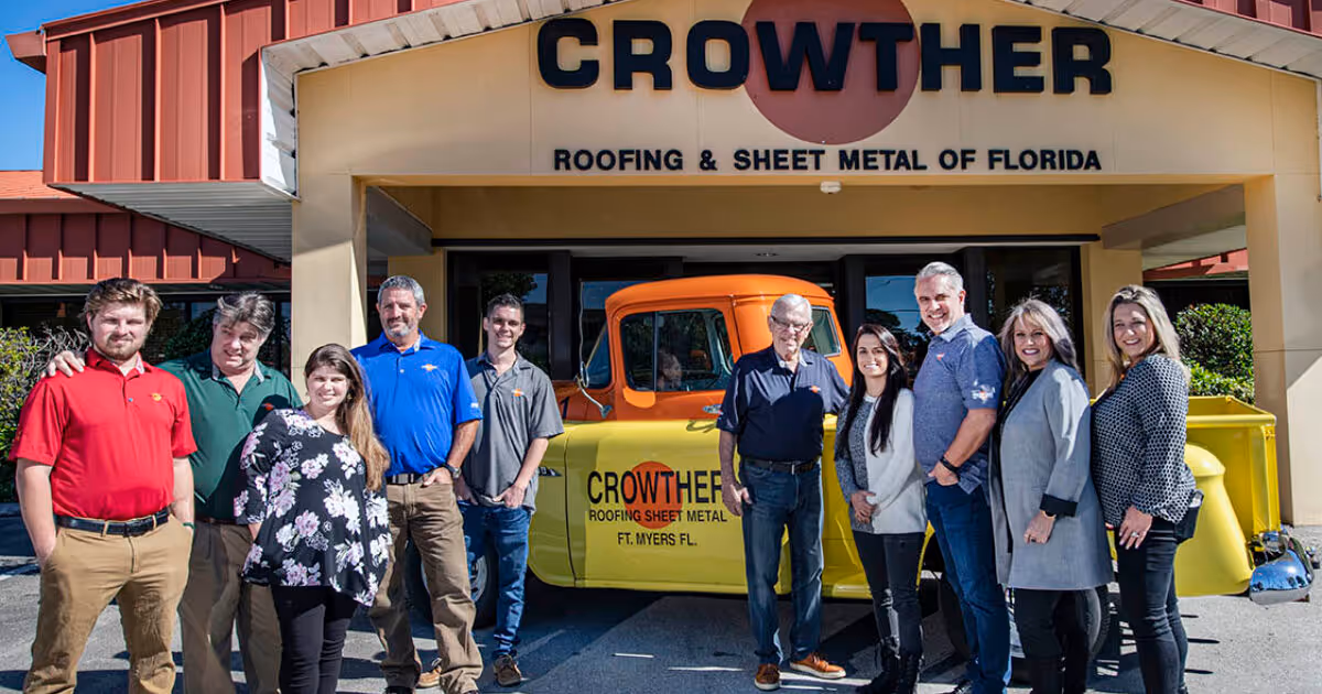 Group of nine people standing in front of Crowther Roofing & Sheet Metal building with a yellow and orange company pickup truck.