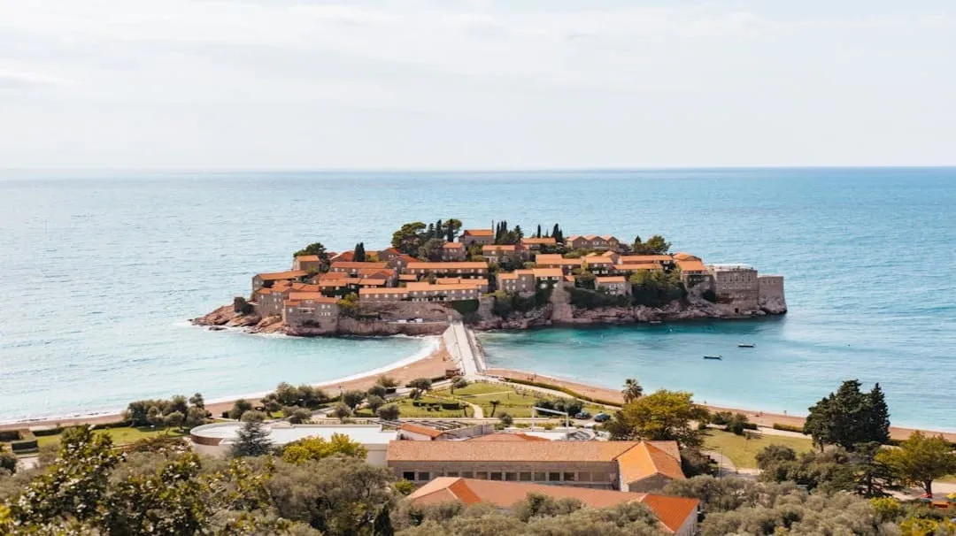 A small island with orange-roofed buildings connected to the shore by a narrow land bridge.