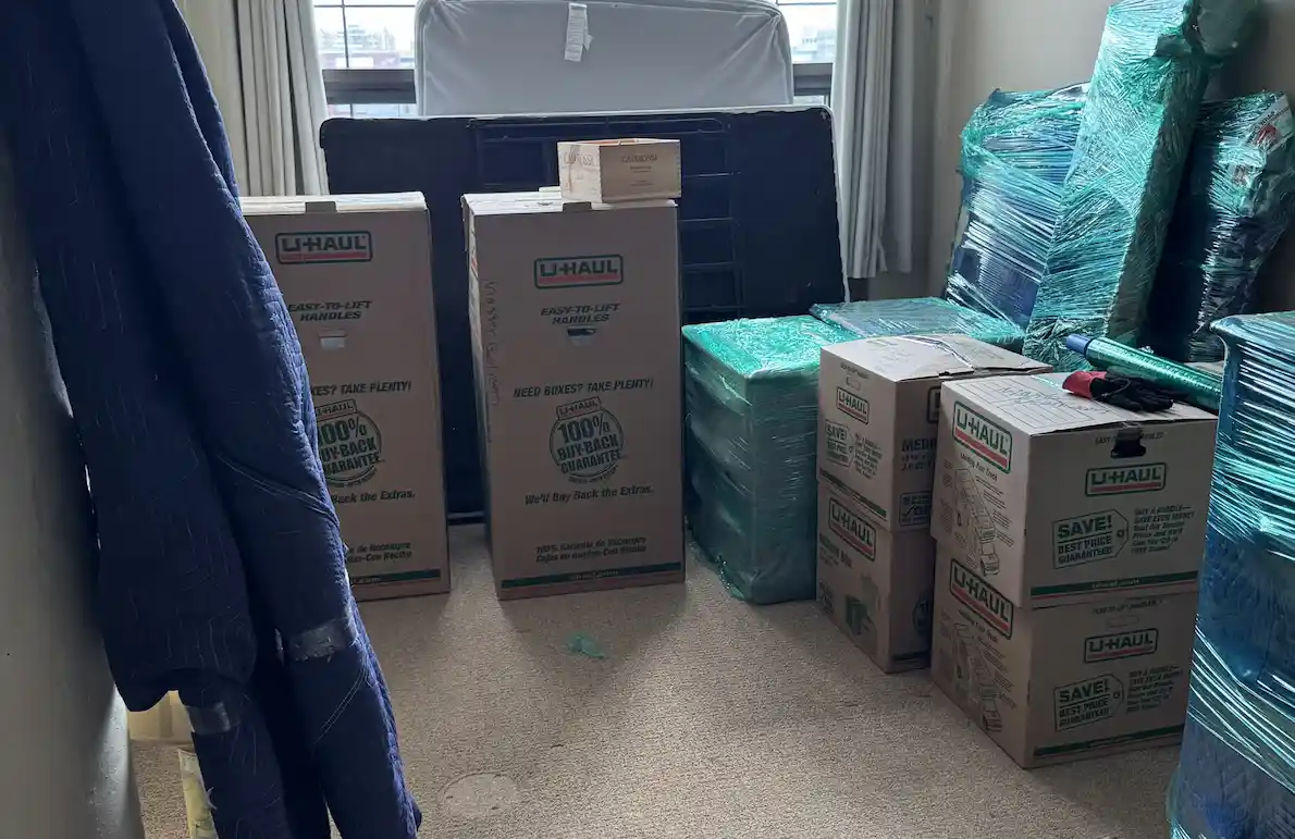 Room filled with U-Haul boxes, wrapped furniture, and moving blankets near a large window for local moving  in Buffalo, NY