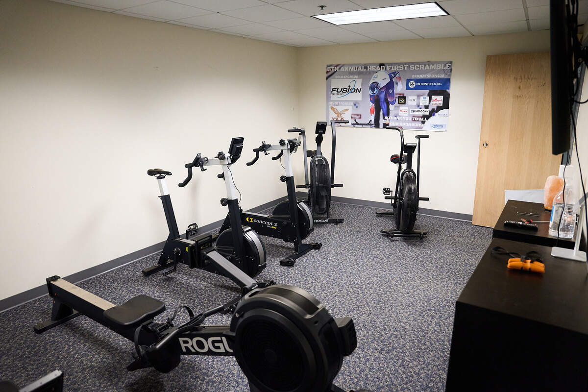 Small exercise room with rowing machine, two stationary bikes, and two air bikes against beige walls.