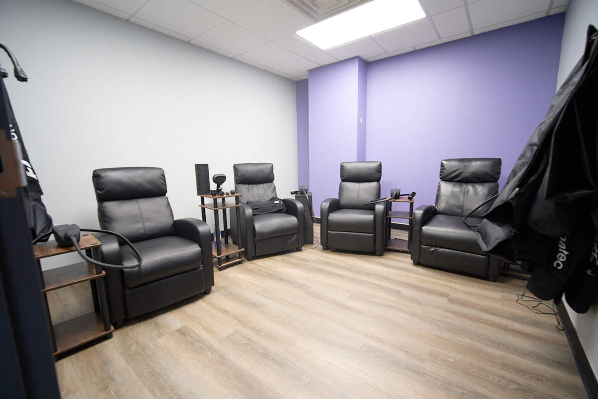 Four black leather recliners spaced apart in a clean room with purple and white walls and wood floor.