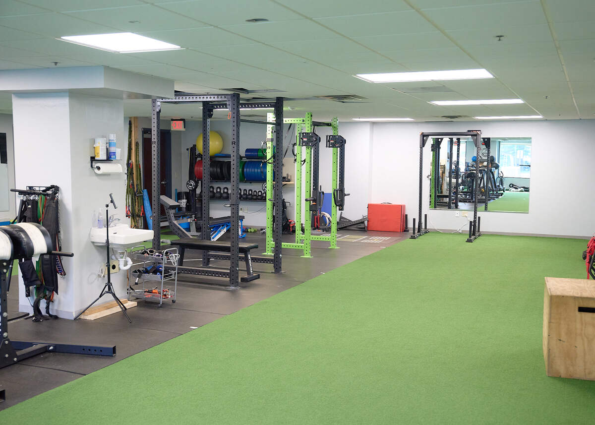 Spacious gym with green turf, weight racks, benches, equipment, and a large wall mirror.