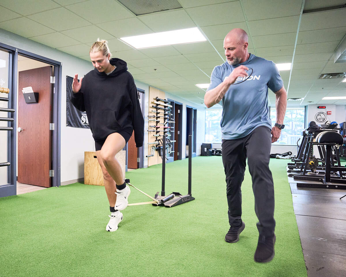 Trainer guiding a woman using resistance bands on her ankles during a workout in a gym.