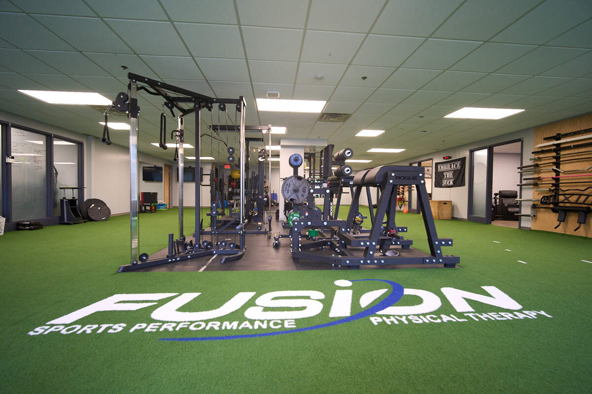 Modern gym room with workout equipment on green turf with Fusion Sports Performance logo.