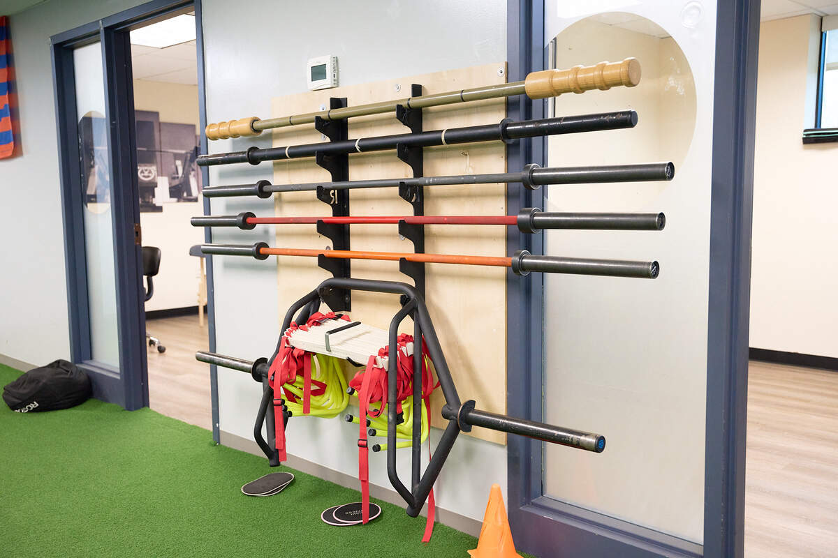 Wall rack holding various barbells and resistance bands in a gym with green turf floor.