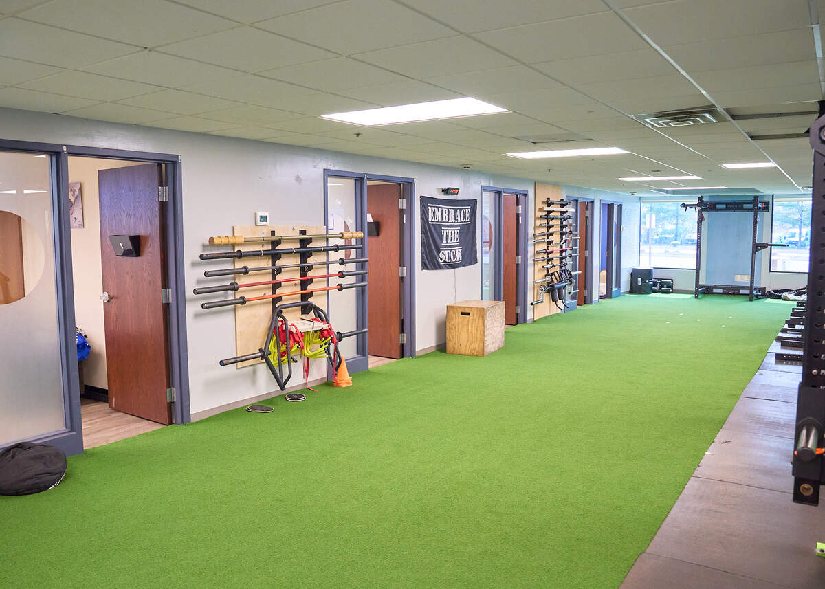 Training room with green turf, weightlifting bars on walls, wooden plyometric box, and fitness equipment.