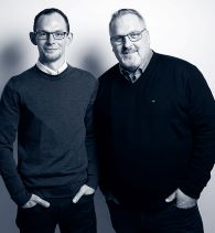 Die Firmengründer von Flethi Gebäudereinigung stehen nebeneinander und lächeln freundlich in die Kamera.