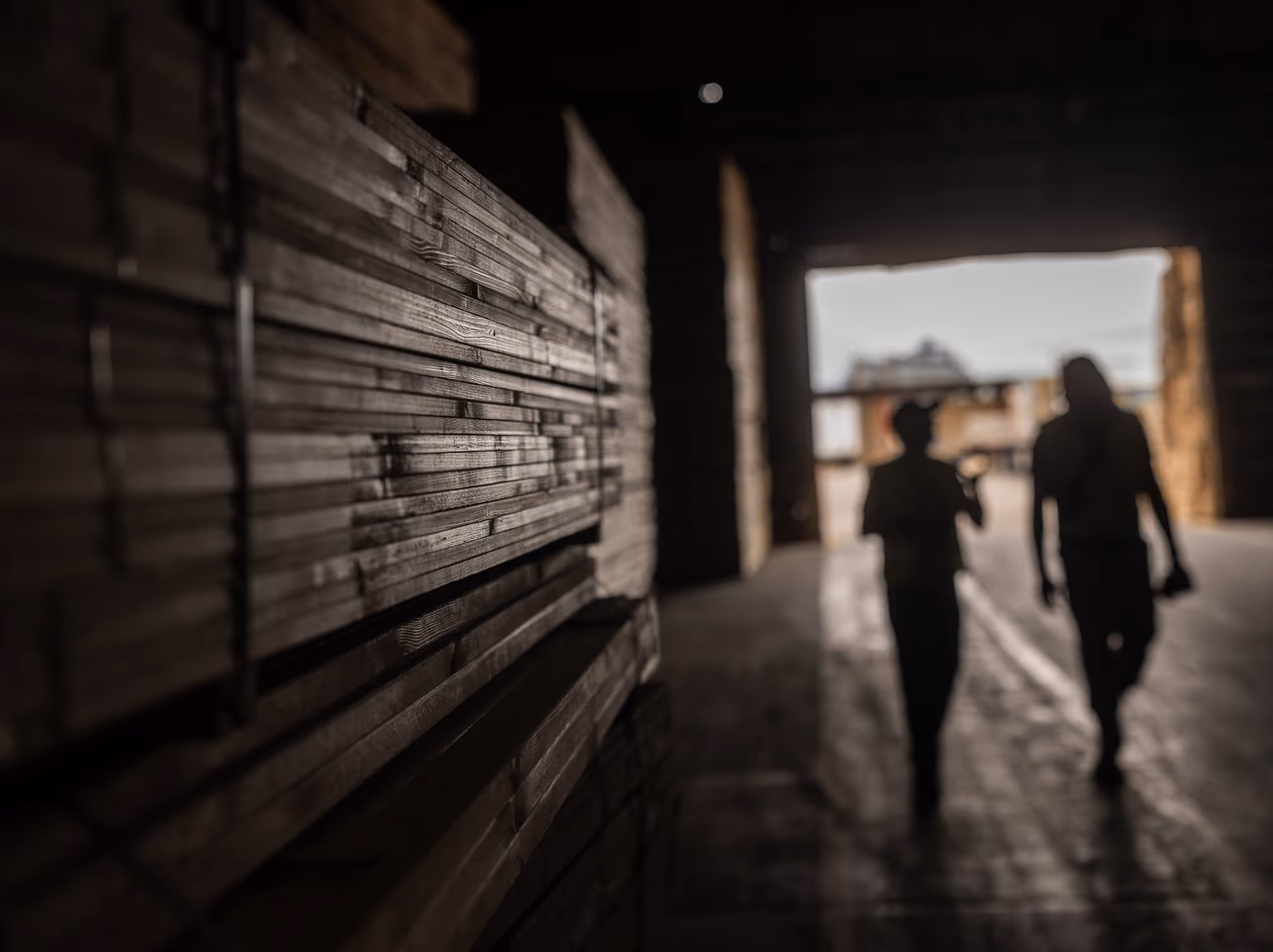 Two people silhoutted walking next to a stack of treated lumber.