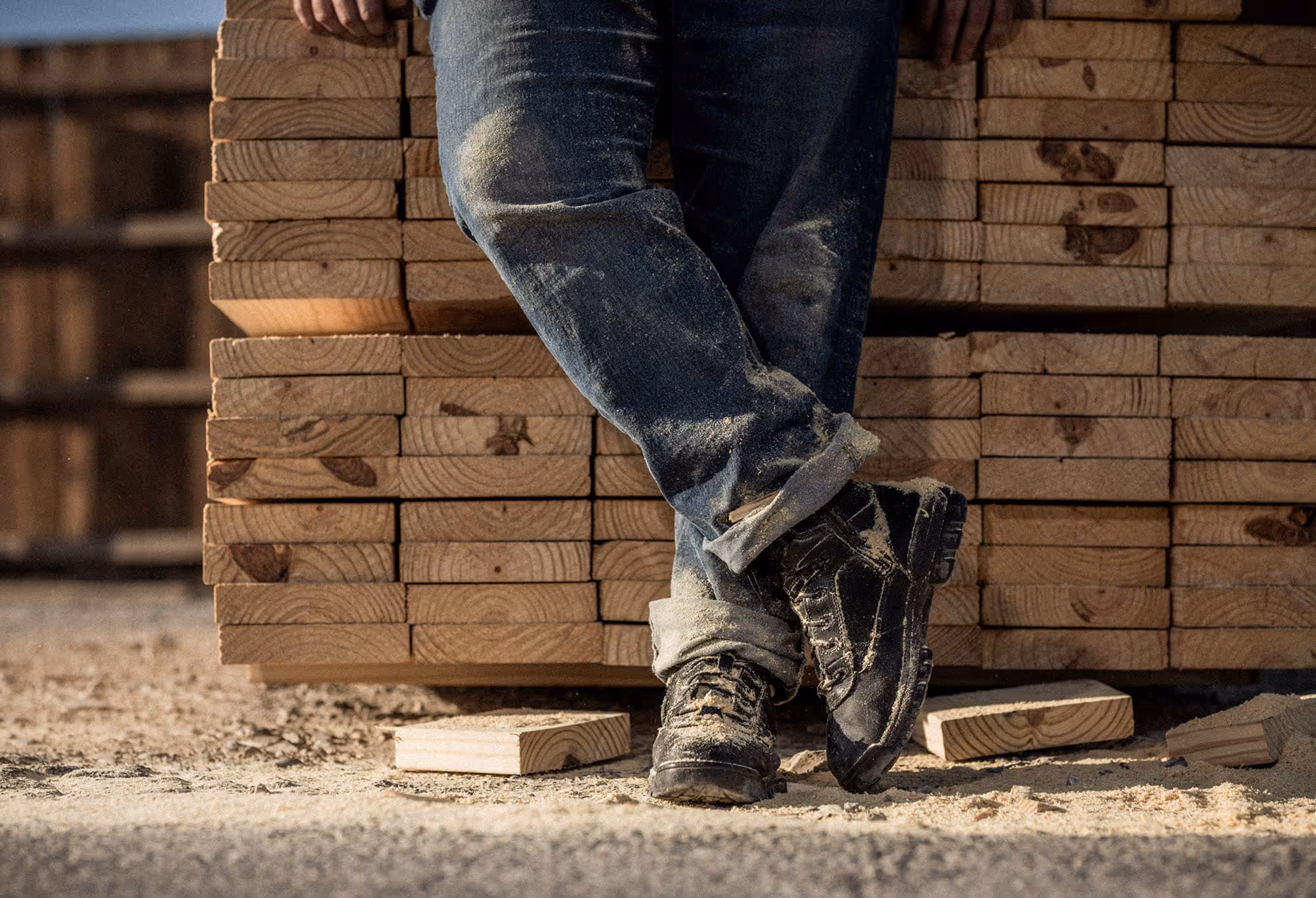 A person's lower half resting against a stack of lumber.