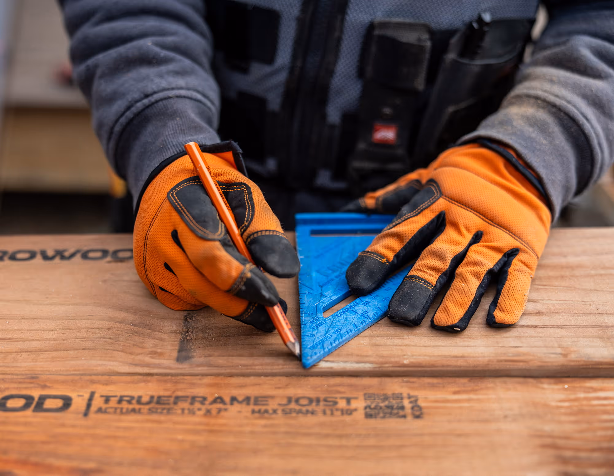 Gloved hands with a triangle and pencil measuring a joist.