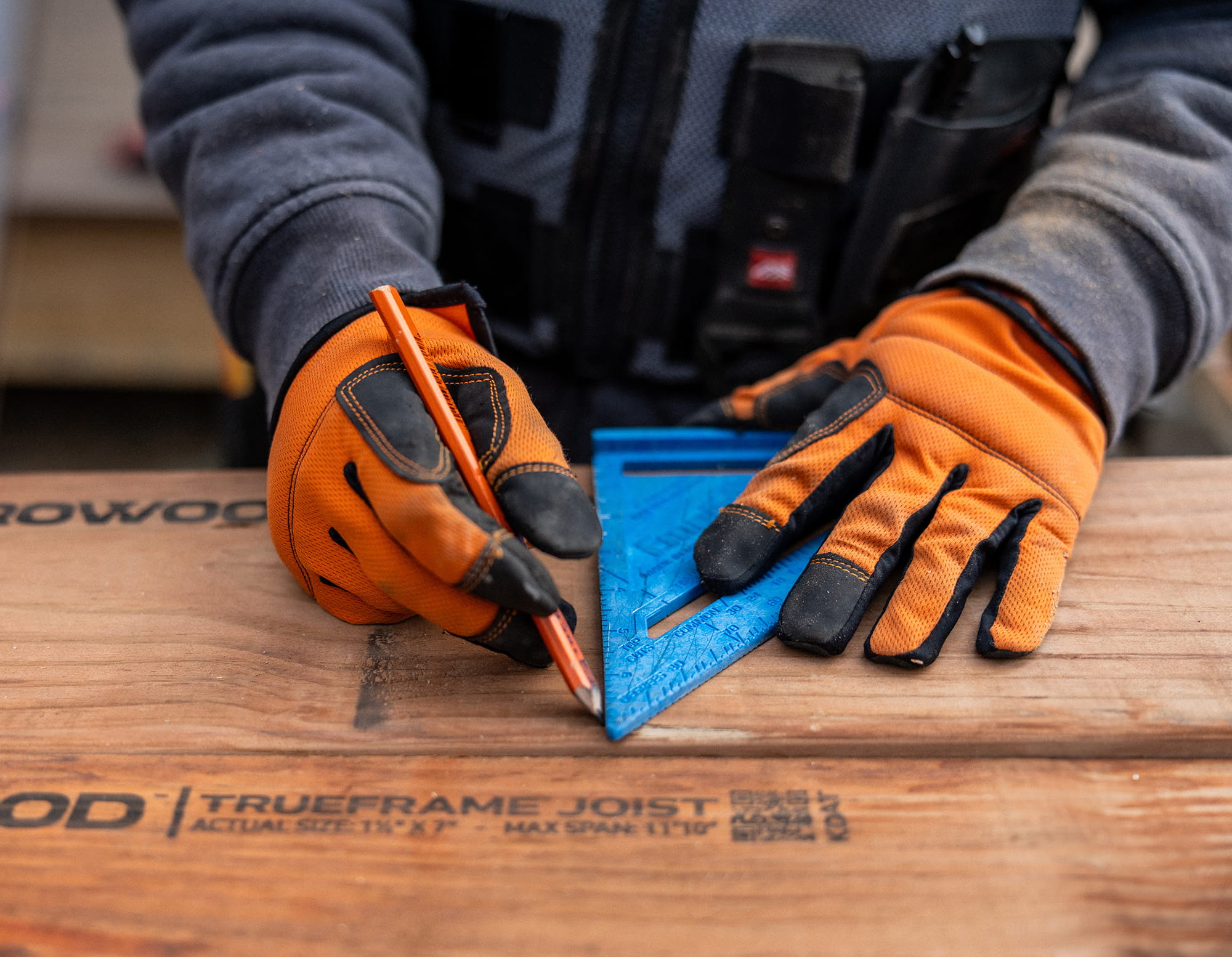 Gloved hands with a triangle and pencil measuring a joist.