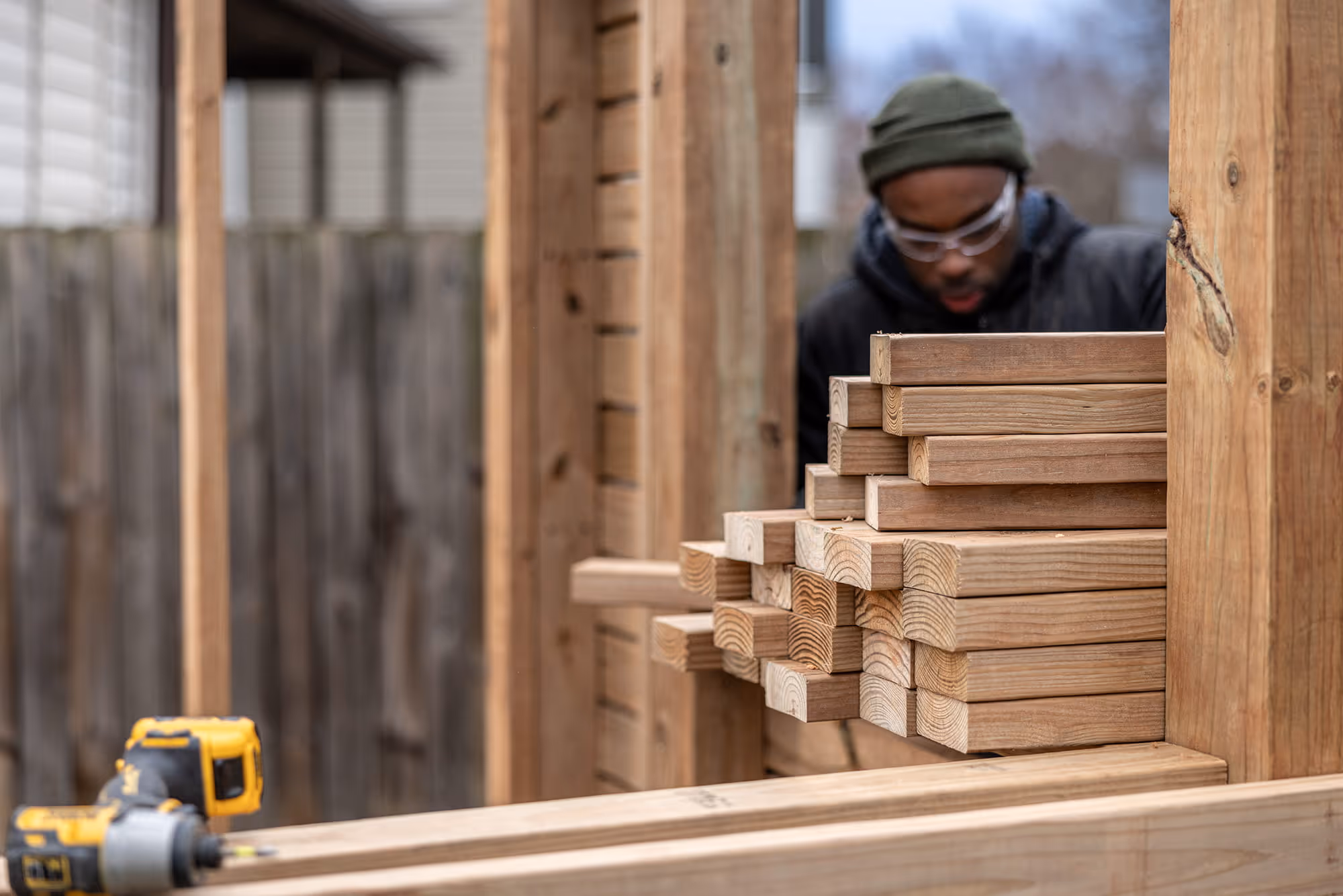 A person stacking 2x4s with a drill in the foreground.