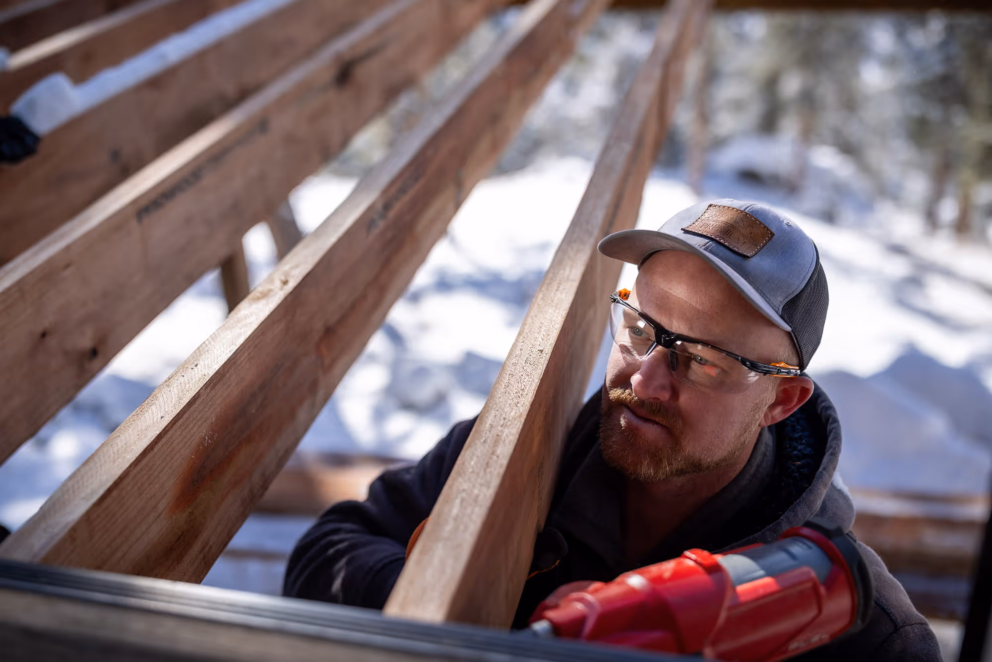 Person using nail gun to hang joist to house while building a 2nd story deck frame.