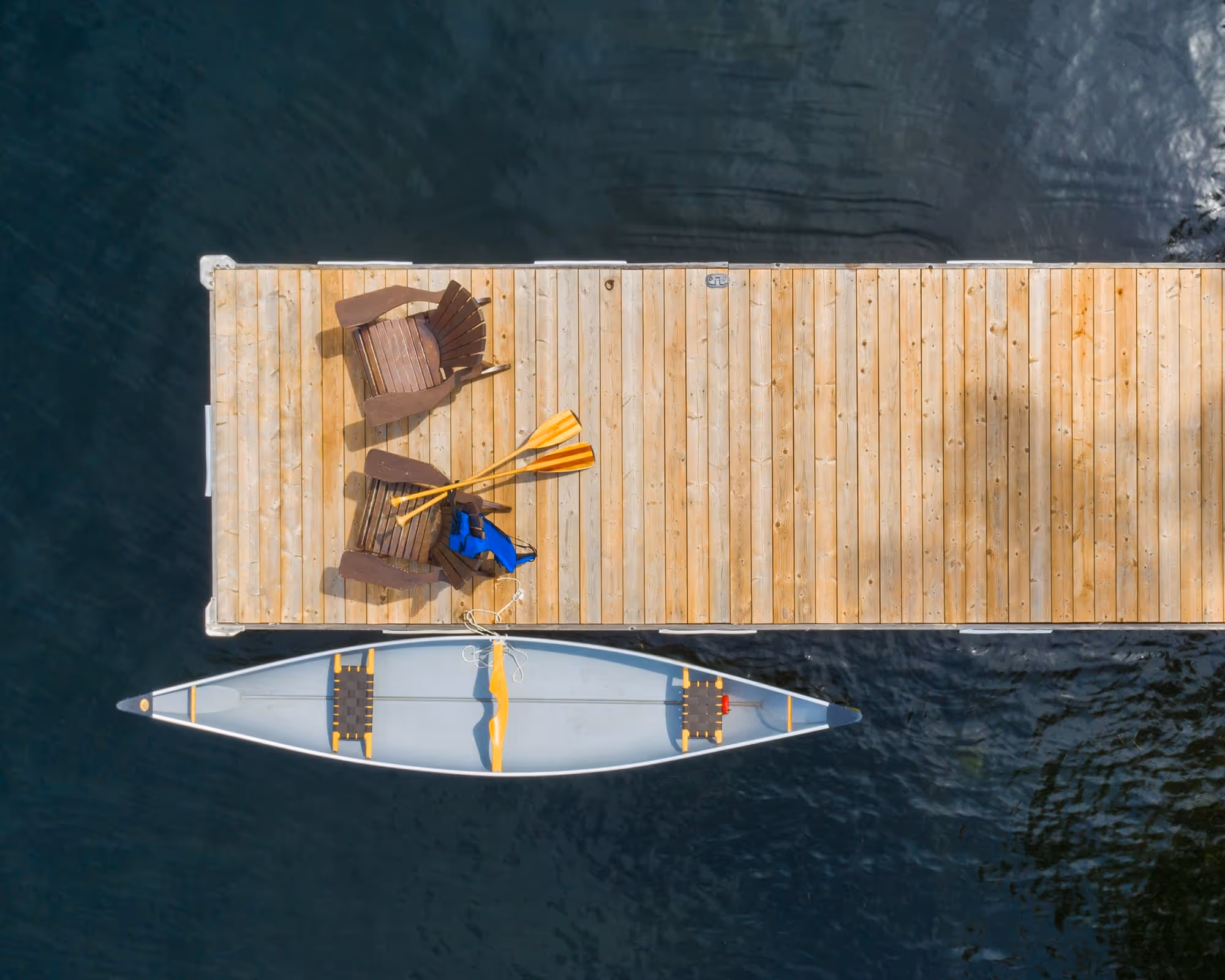 Chairs on a treated lumber dock surrounded by water. A canoe is pulled up to the dock.