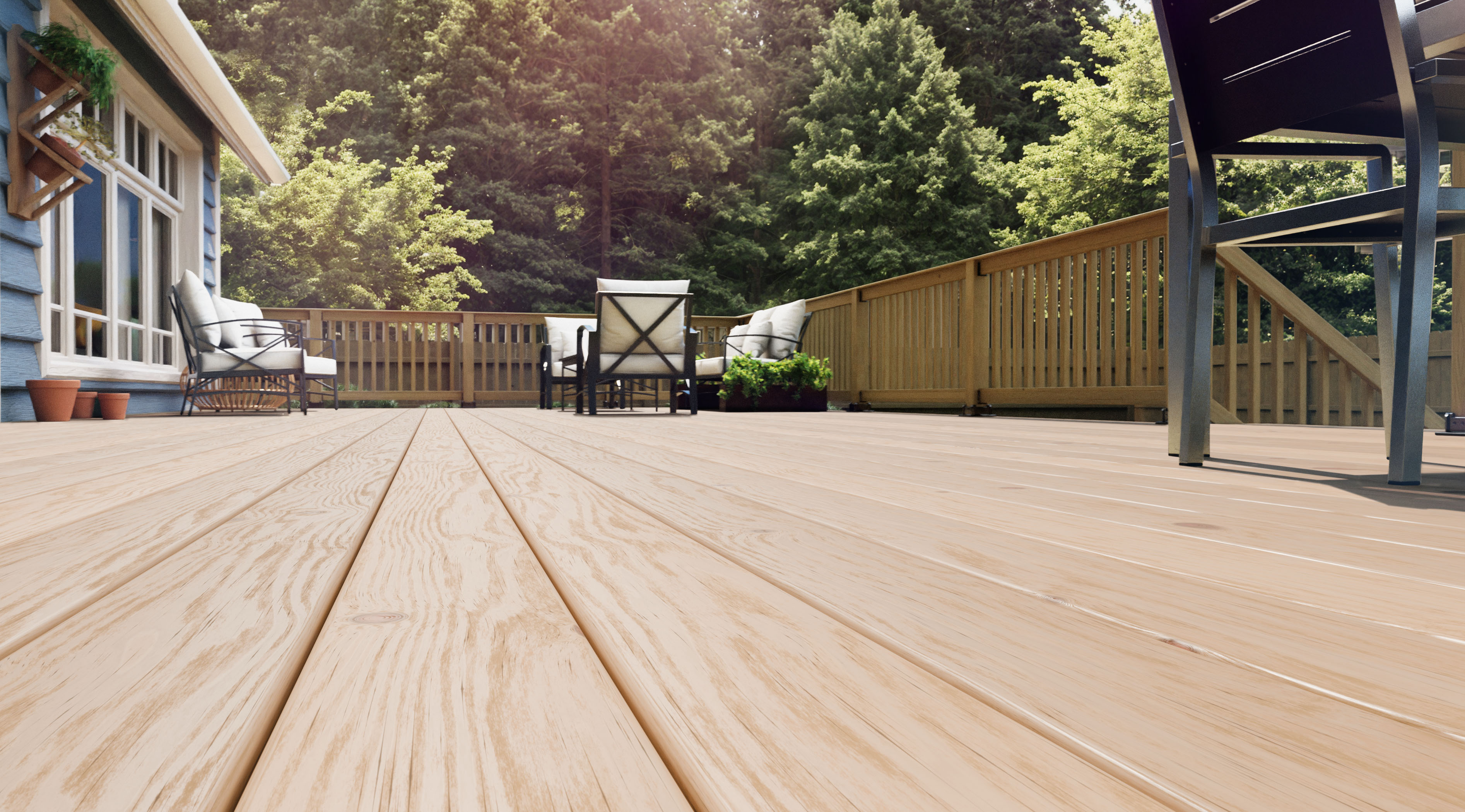 Low-angle view of a spacious wooden deck with outdoor seating and a forested background.
