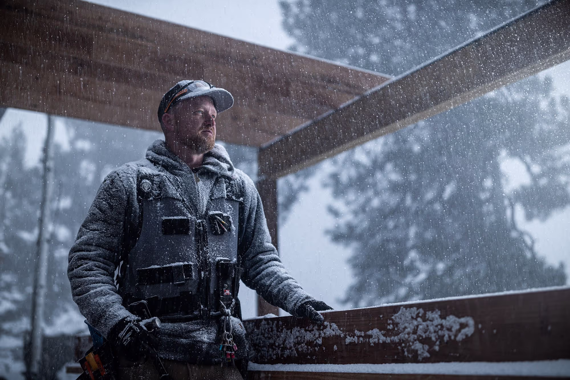 A person standing in front of a TrueFrame Joist with their left hand on the joist while it is snowing heavily.