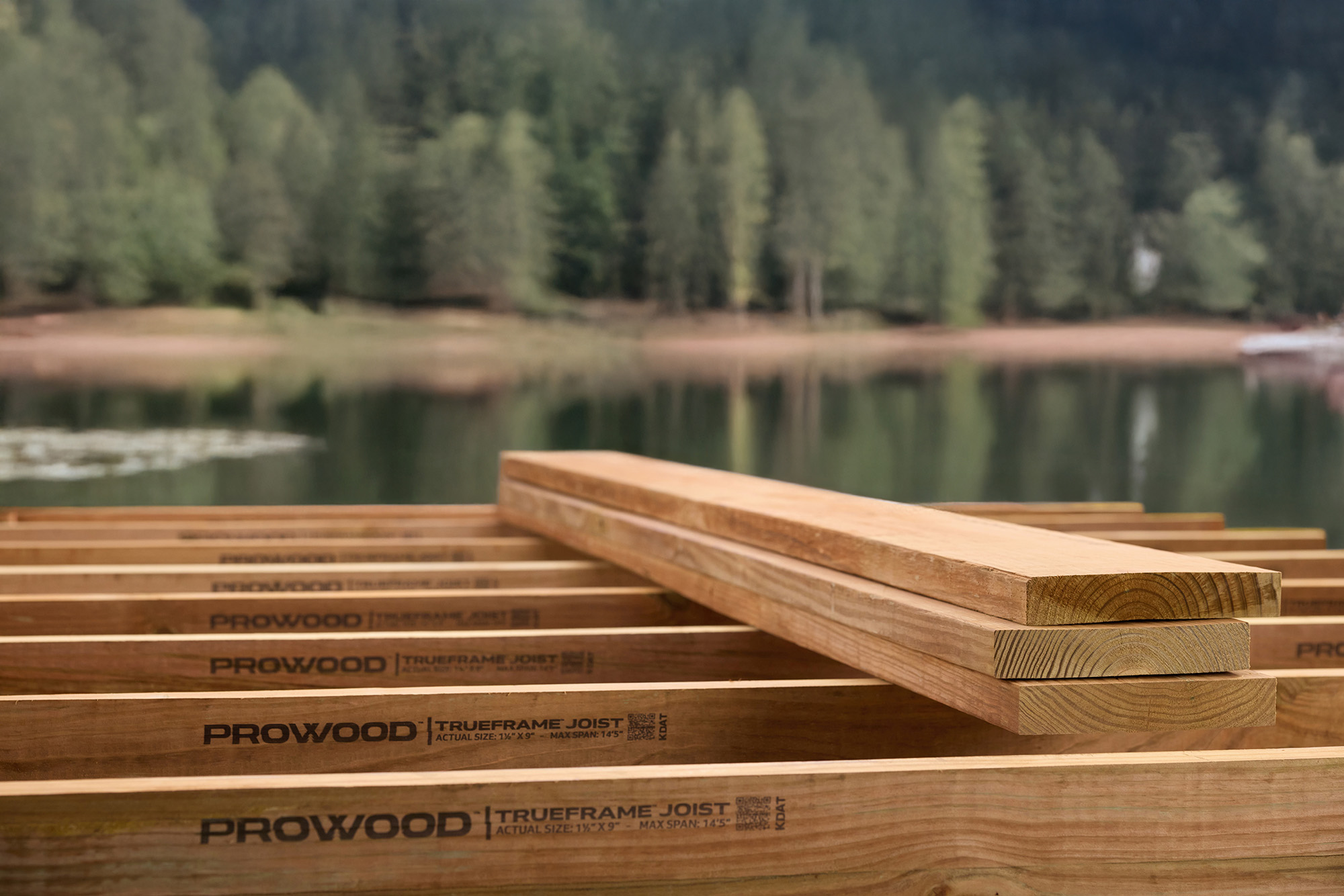 A treated wood deck frame built out of TrueFrame Joists with a lake and trees in the background.