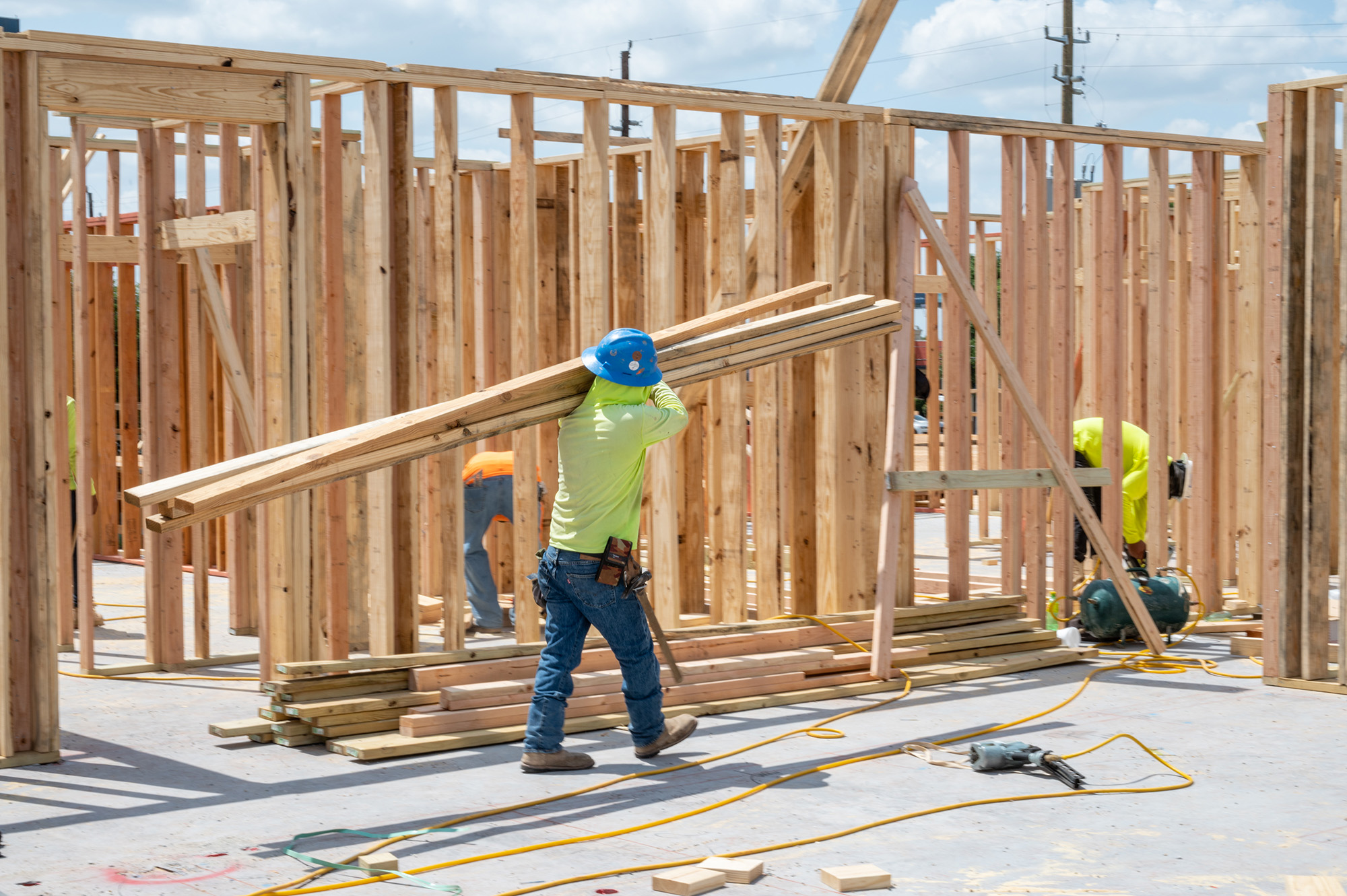 Construction workers in safety gear carrying and working with wooden beams inside a building framework under construction.