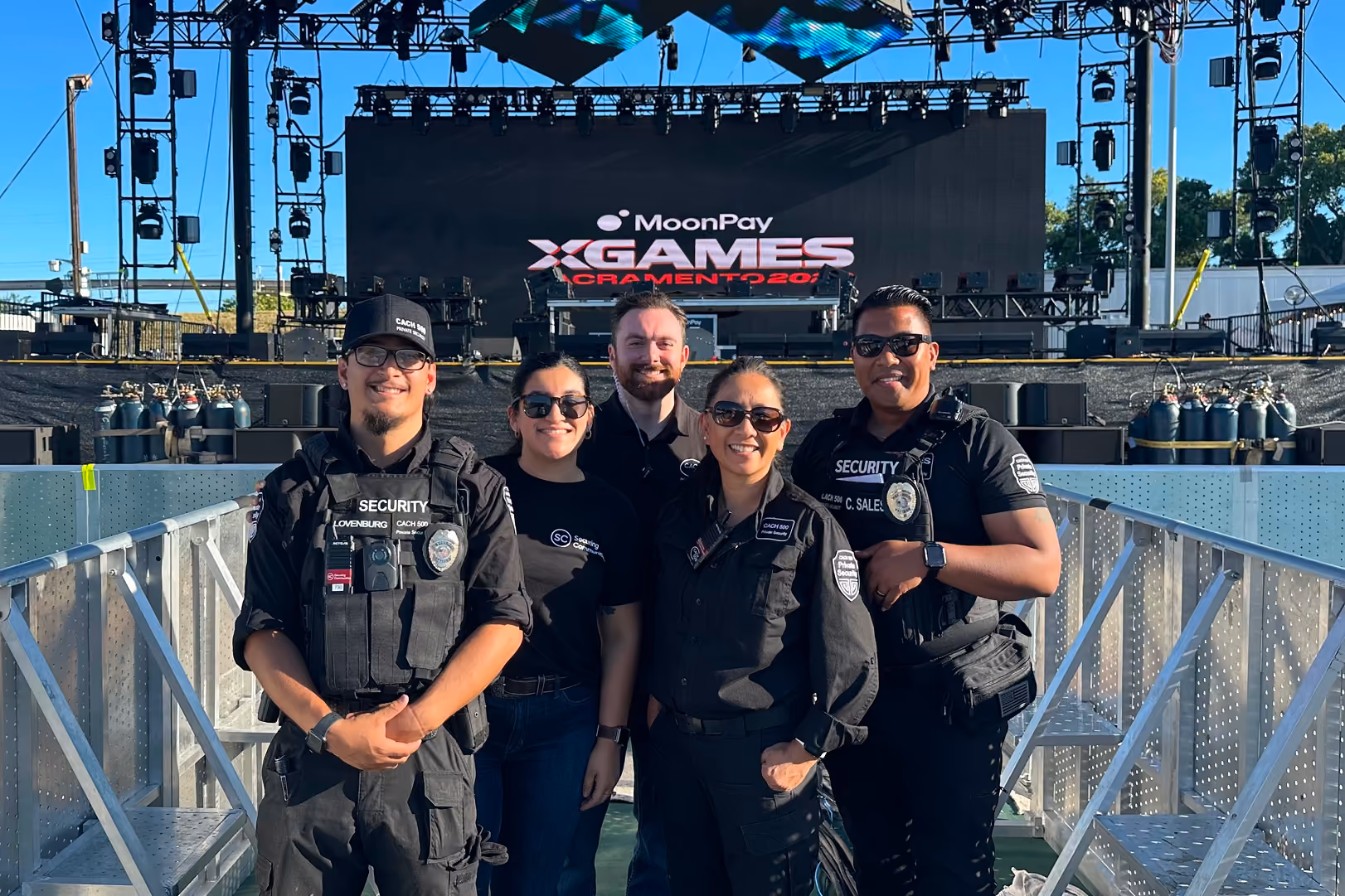 Group of five security and event staff smiling in front of X Games Sacramento stage outdoors.