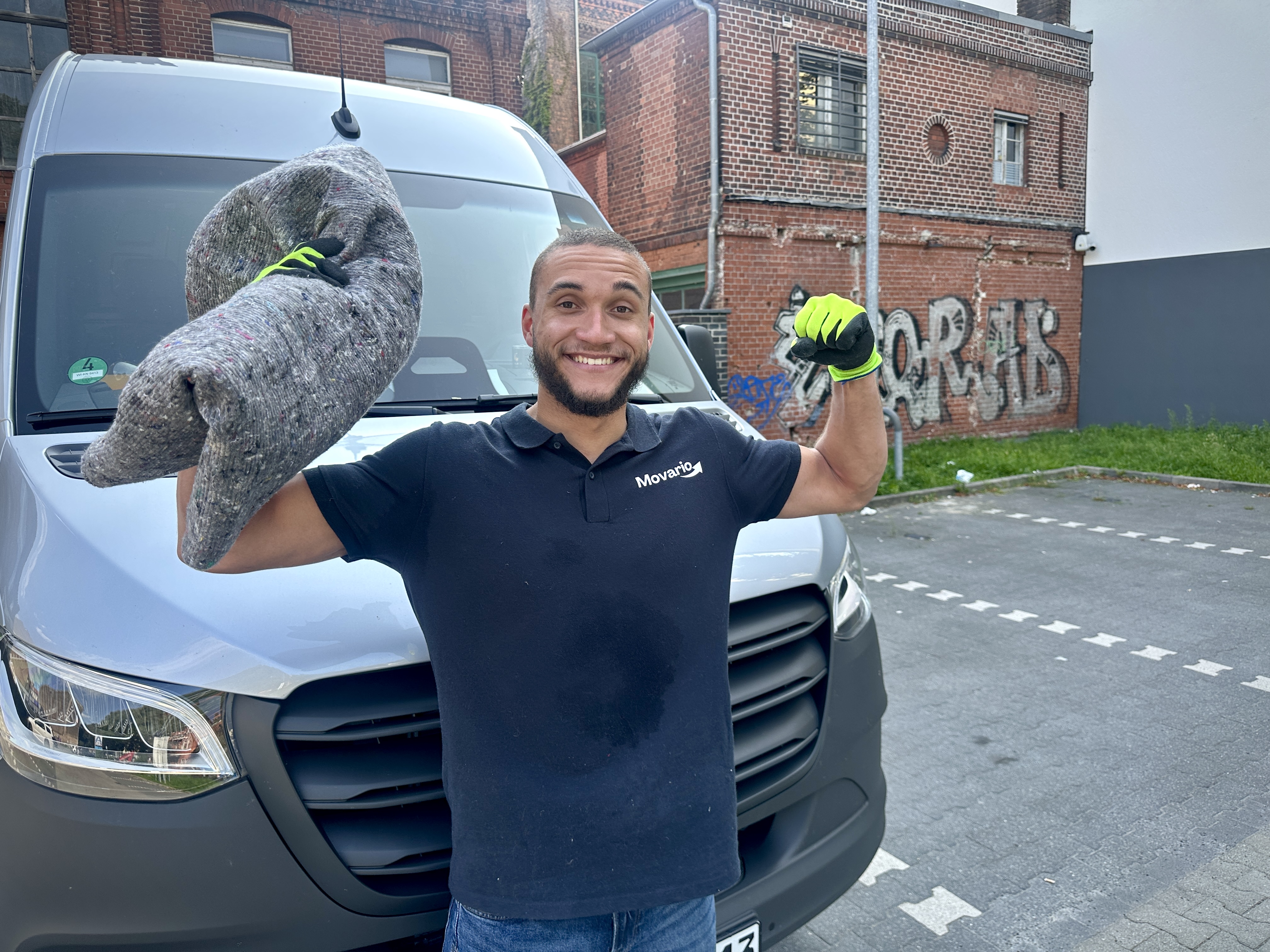 Movario Umzugshelfer steht vor einem Transporter und hält eine blaue Umzugsdecke in der Hand – professioneller Umzugsservice in Berlin