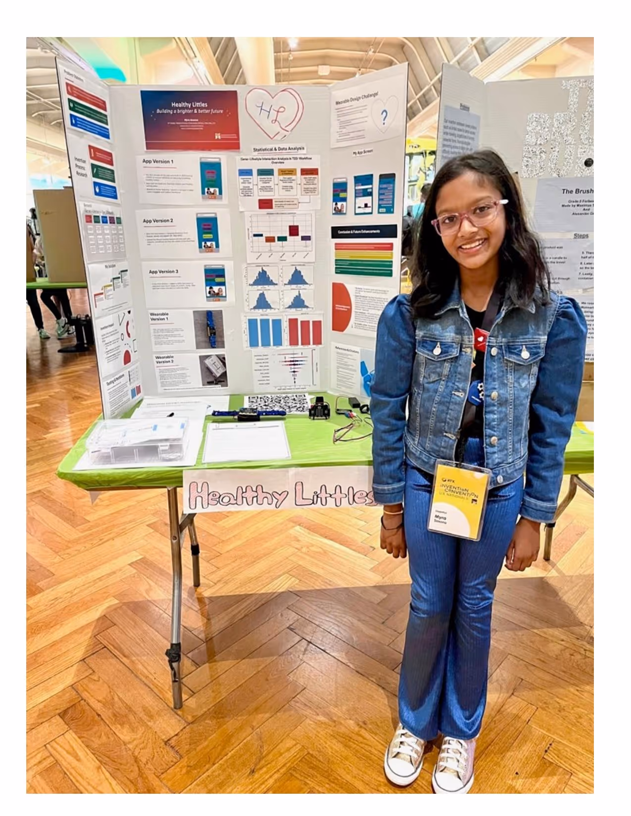 Young girl smiling while standing in front of her invention poster