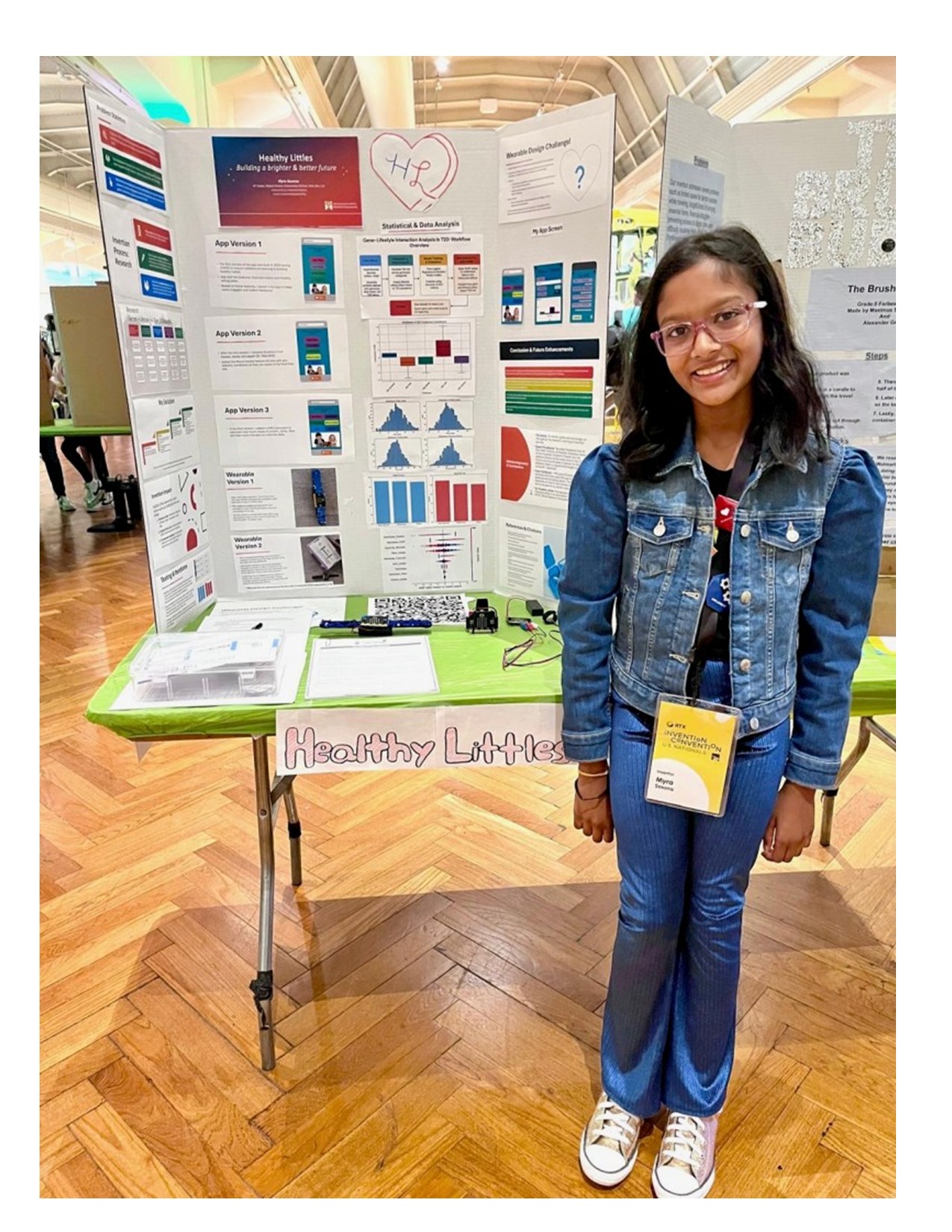 Young girl smiling while standing in front of her invention poster