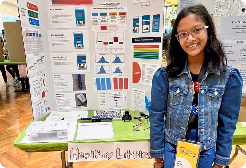 Young girl smiling while standing in front of her invention poster