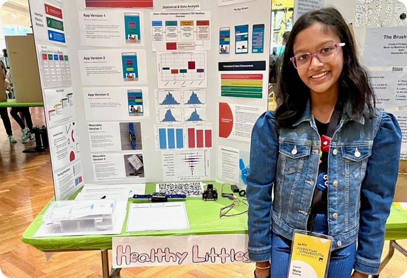 Young girl smiling while standing in front of her invention poster