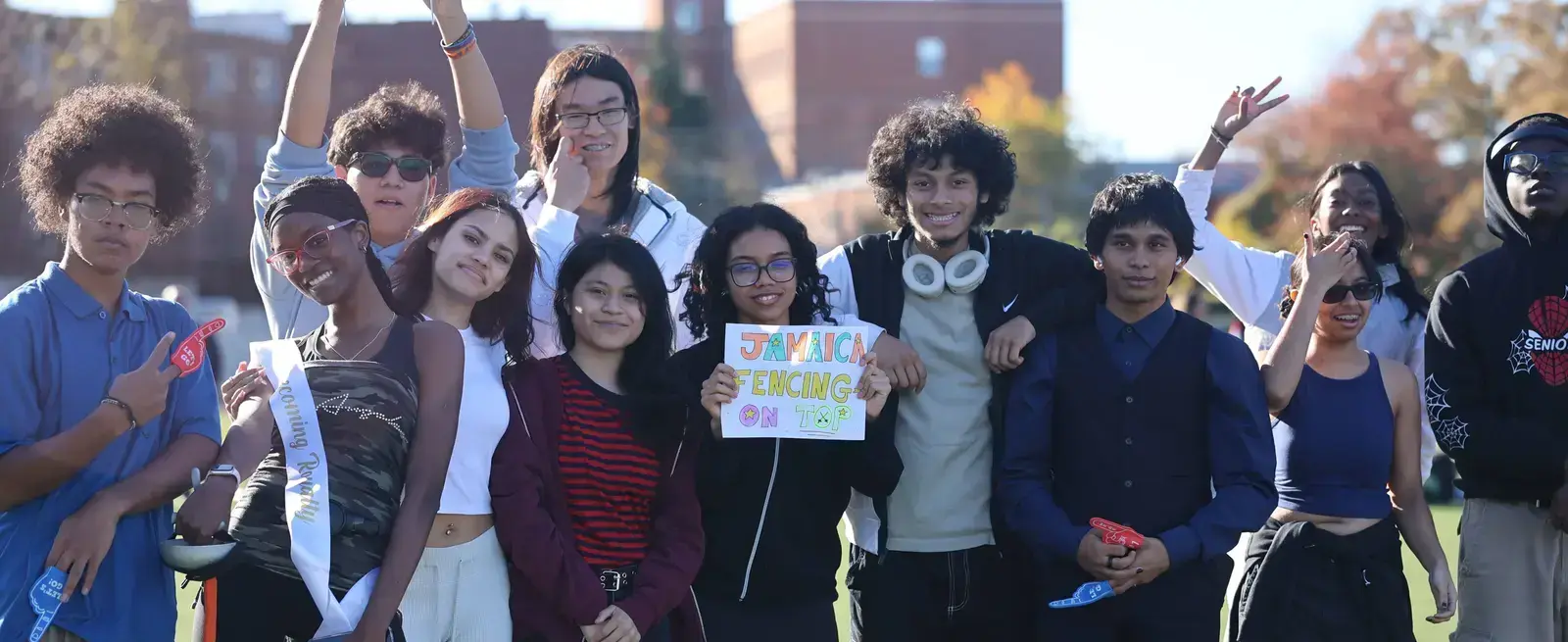 Students cheering outdoors holding a Jamaica Fencing sign
