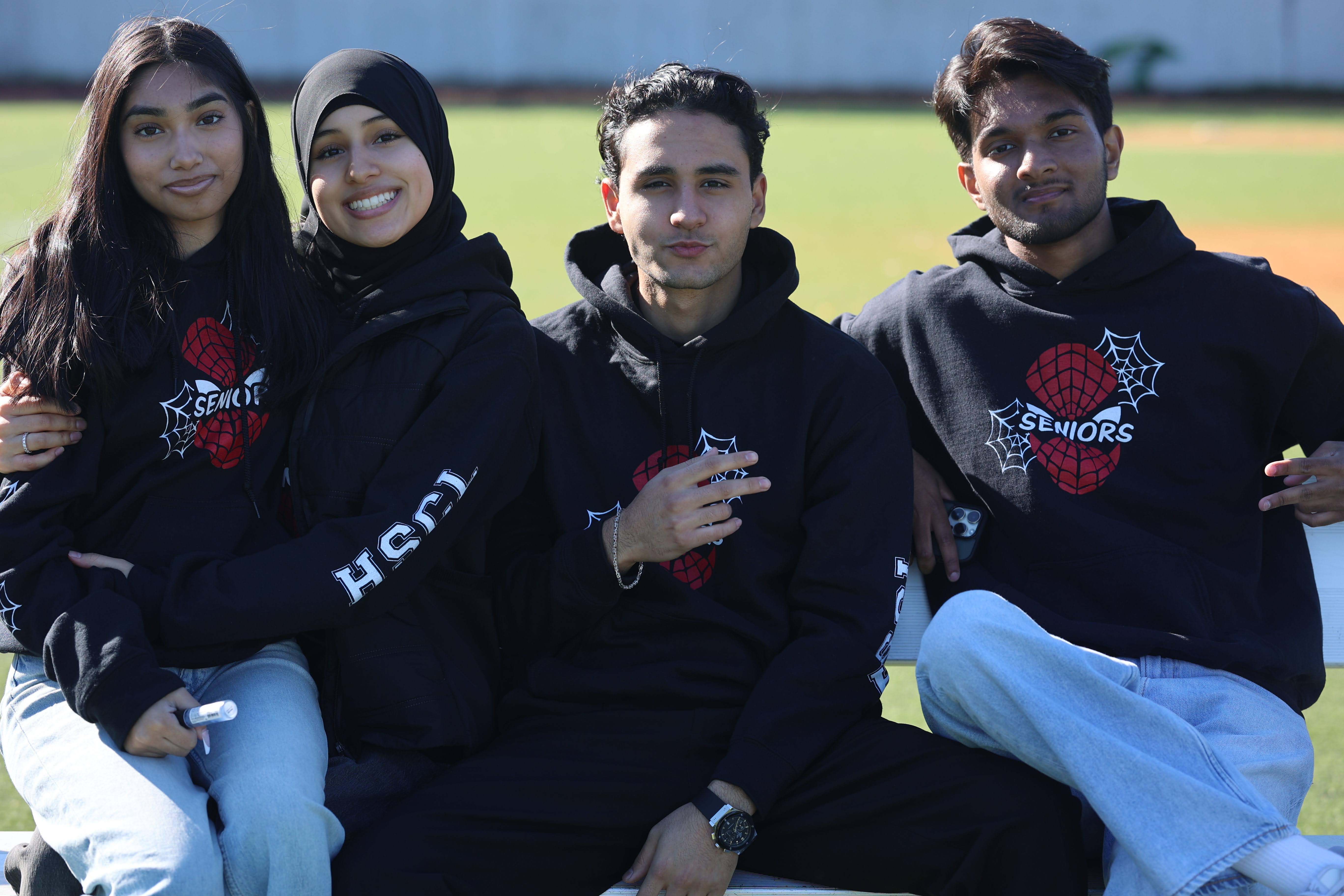 Four high school seniors wearing matching black Seniors hoodies outdoors