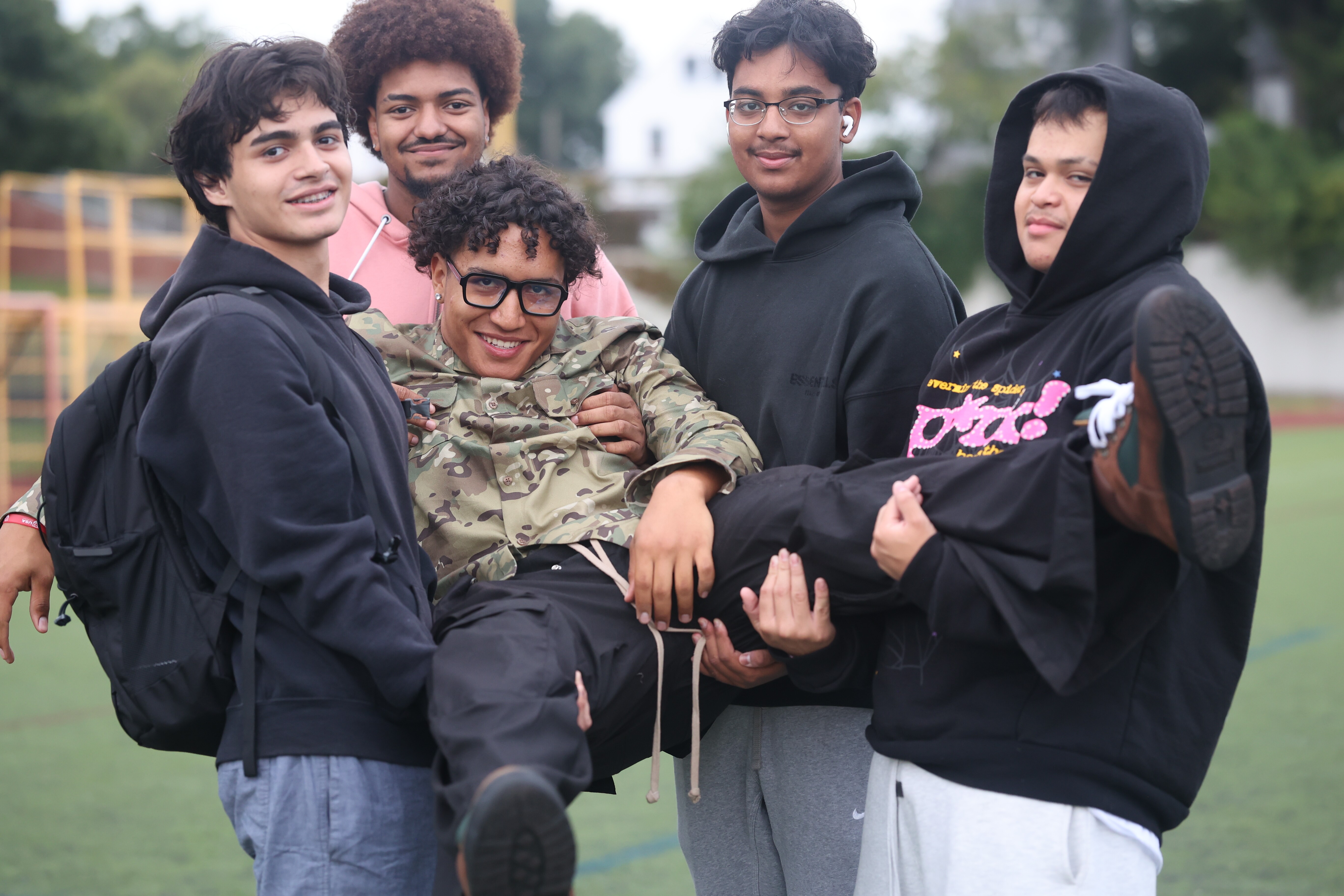 Five high school students laughing together on an outdoor athletic field