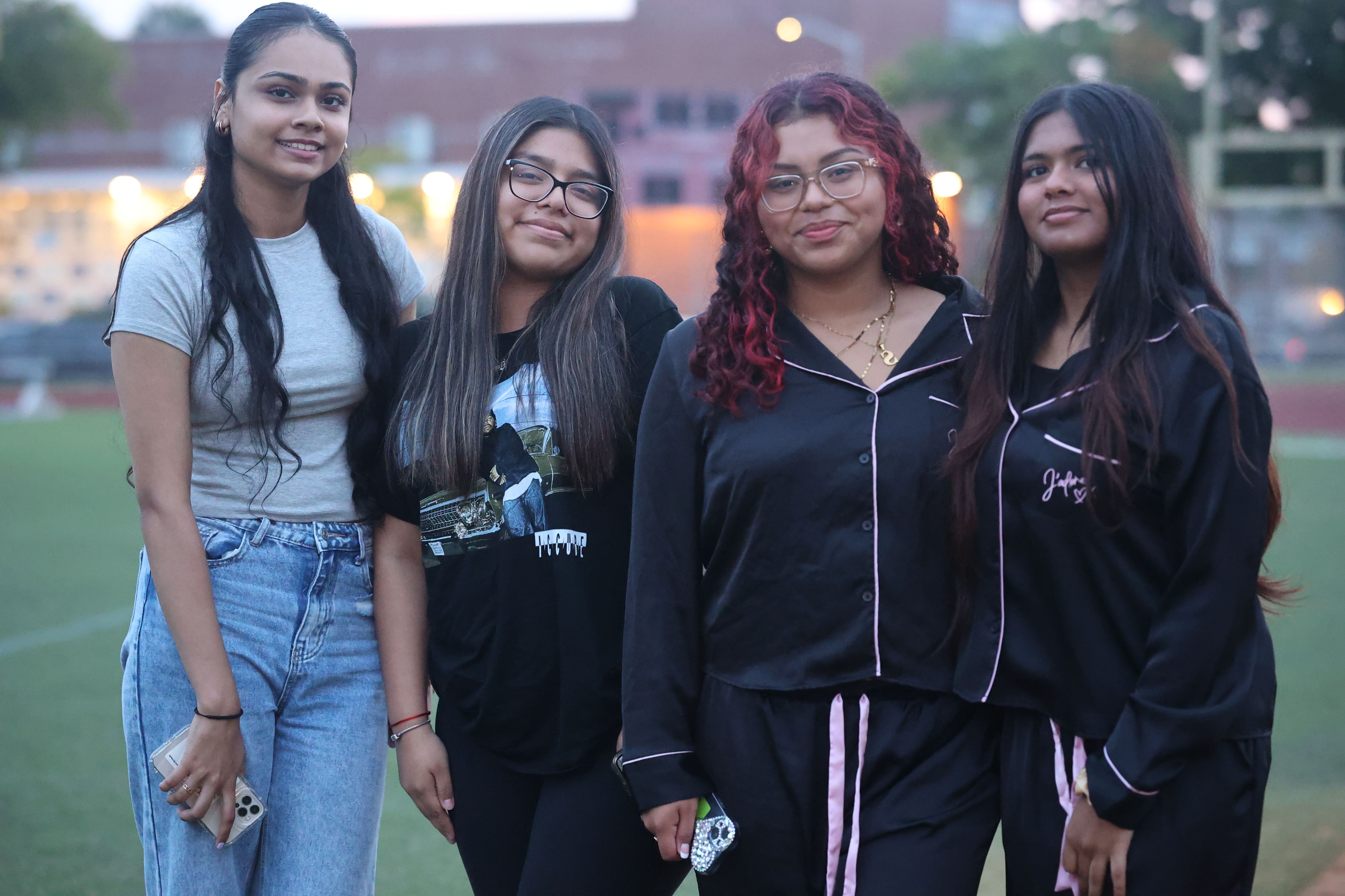 Four female students smiling together on school athletic field at dusk