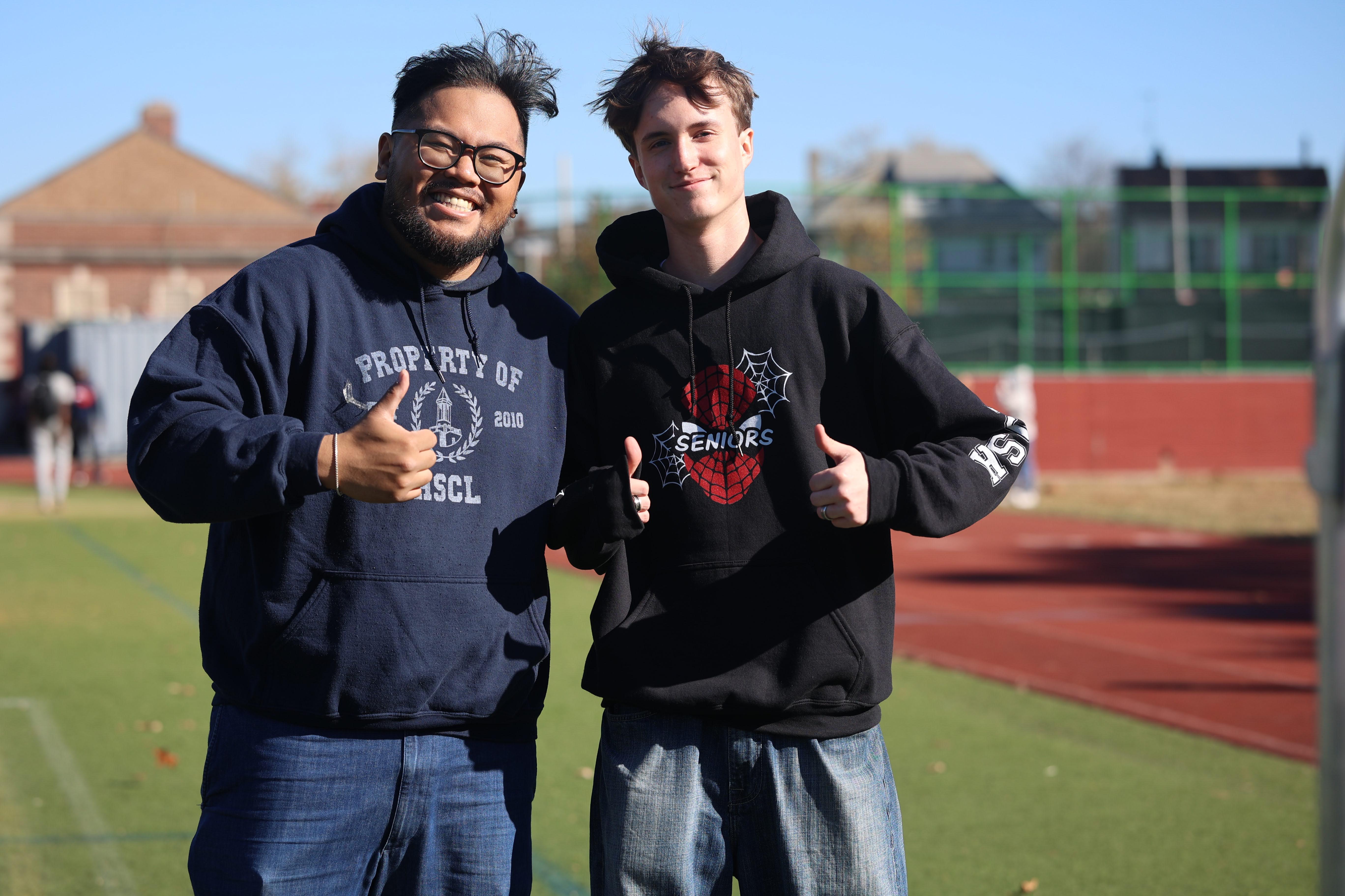 Two smiling students giving thumbs up on school athletic field