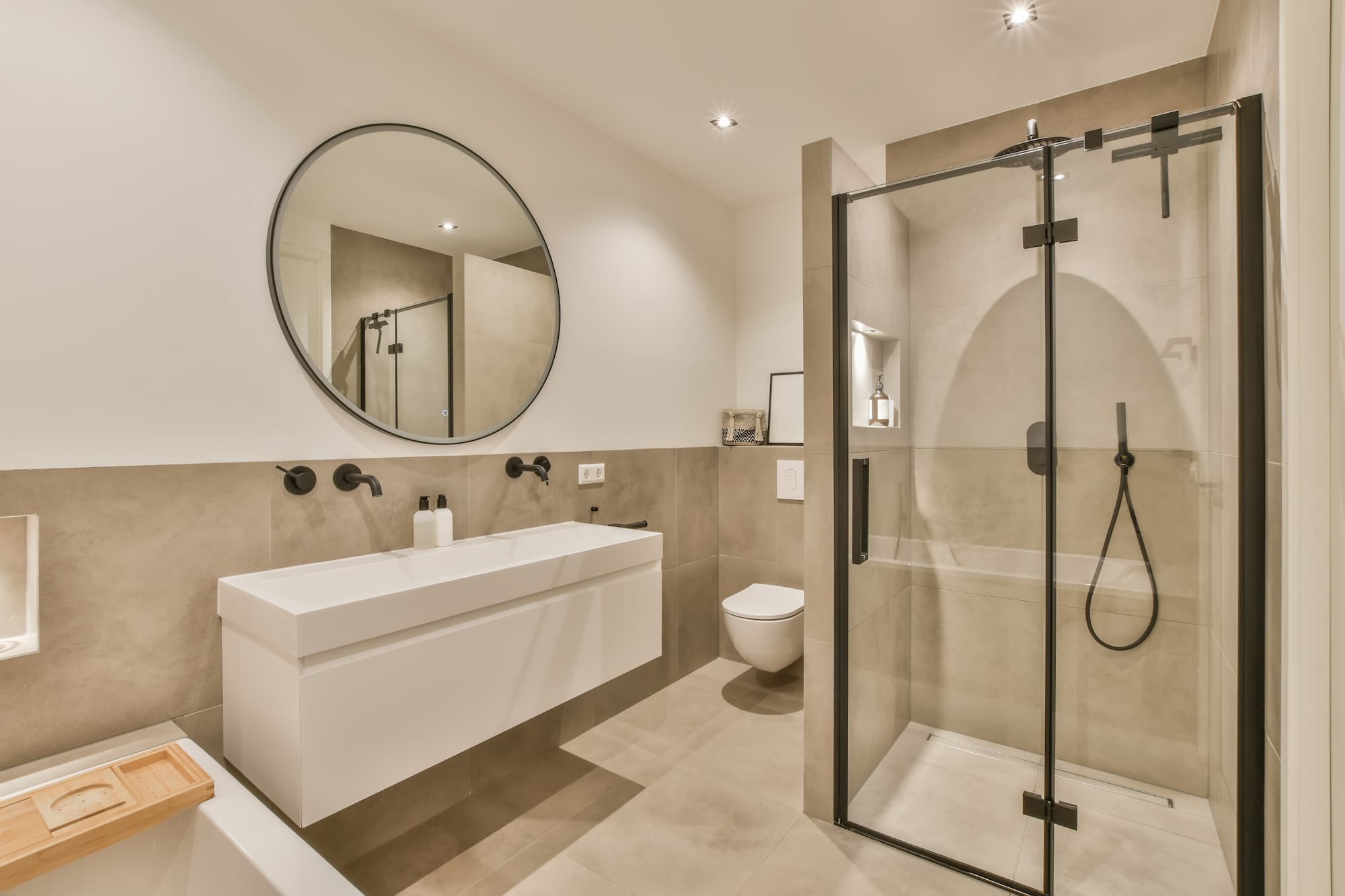 Salle de bain moderne avec lavabo blanc suspendu, grand miroir rond, douche à paroi en verre et toilettes suspendues. Photographie immobilière - Hôtel salle de bain spacieuse