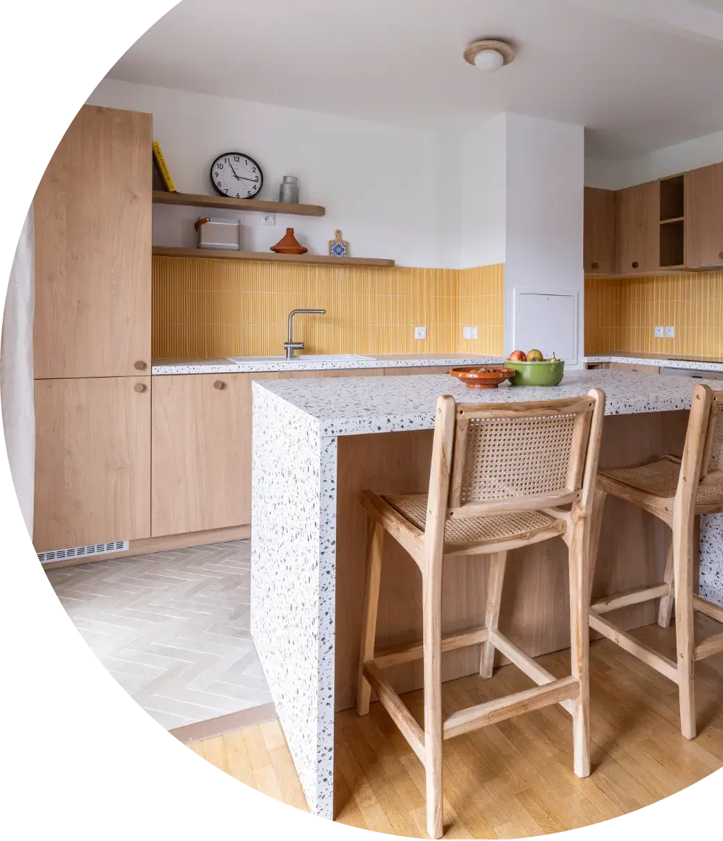 Leur conceptrice, Manon, a donc imaginé une cuisine ouverte en L avec un îlot central pour faciliter la circulation, gagner en rangement et obtenir un rendu plus épuré. Les choix se sont faits naturellement: façades en chêne miel, plan de travail en granito beige et crédence jaune pour apporter chaleur, lumière et personnalité. La cuisine réutilise aussi l’électroménager existant, parfaitement intégré pour une démarche durable.