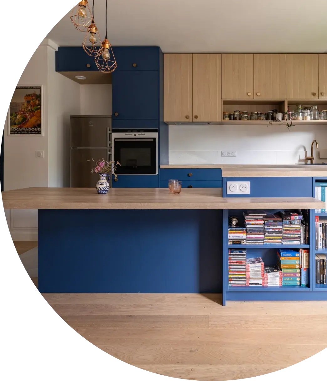 L’objectif était clair : optimiser l’espace et rassembler au même endroit la cuisine, la salle à manger et un espace de travail occasionnel. Amateurs de lecture, ils avaient besoin de nombreux rangements, dont des niches pour garder leurs livres à portée de main. Dès le départ, ils avaient une idée précise des couleurs, avec une cuisine bicolore mêlant bleu éclipse et chêne clair. Accompagnés par leur conceptrice Florence et leur artisan-poseur, le projet a évolué jusqu’à intégrer une table permettant d’accueillir jusqu’à six personnes, ainsi qu’un élégant retour tablette dans le prolongement de l’îlot.