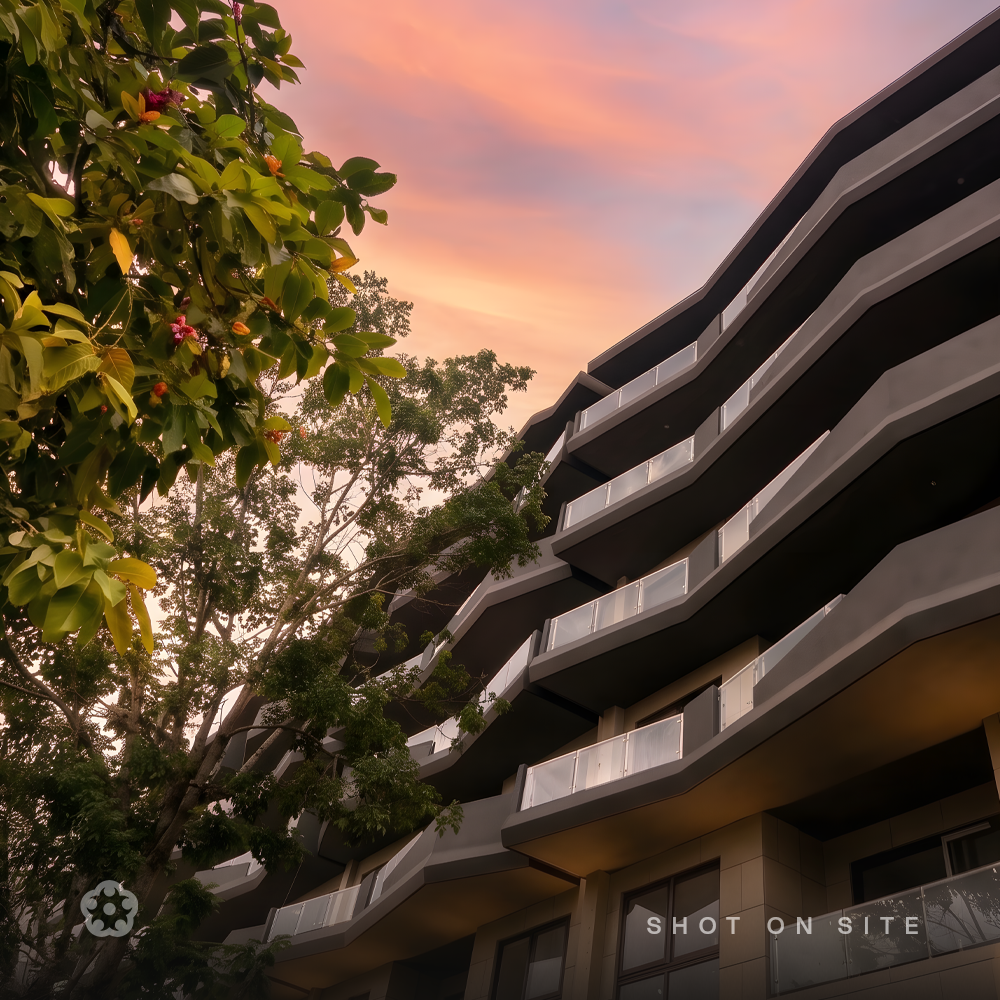 Upward view of stepped cantilevered balcony geometry framed by an existing tree retained in the structural site layout at a JRC Projects community, Sarjapura Road