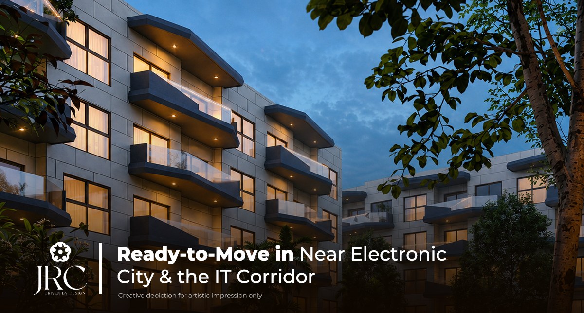 Low-rise apartment blocks at JRC Wildwoods lit at dusk and framed by mature trees — ready-to-move 3 BHK lakefront flats off Sarjapur Road, about fifteen minutes from Electronic City, Bangalore