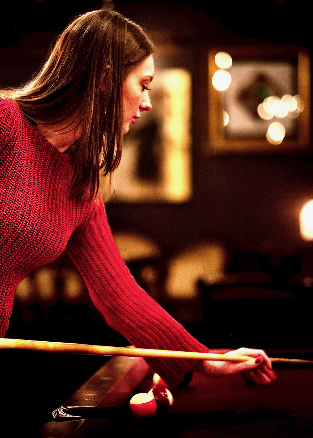 Brunette woman peering over the pool table, examining her shot