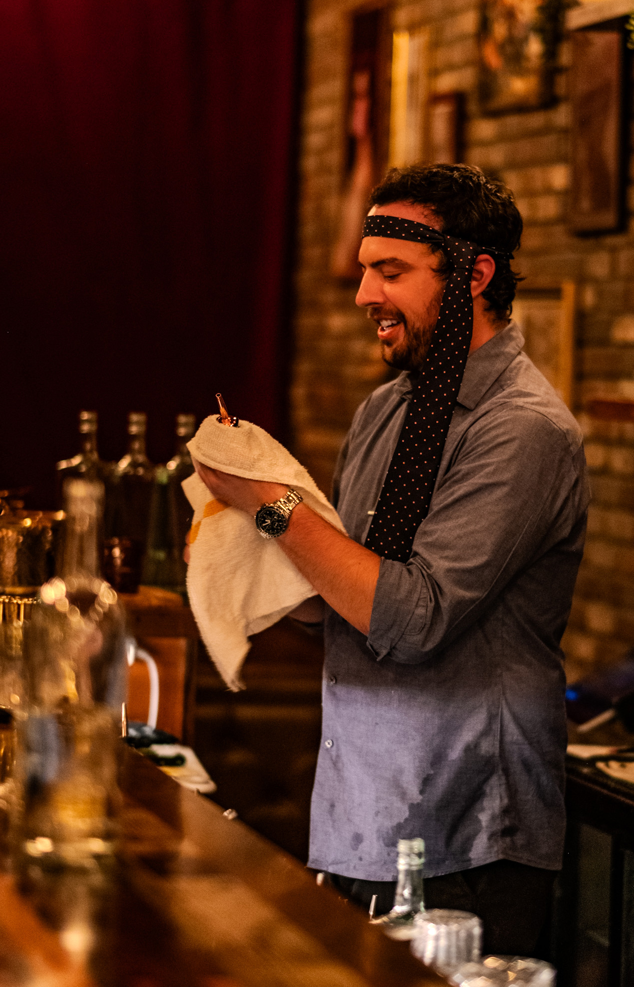Bartender Jordan wearing a tie around his head like a ninja polishing glassware
