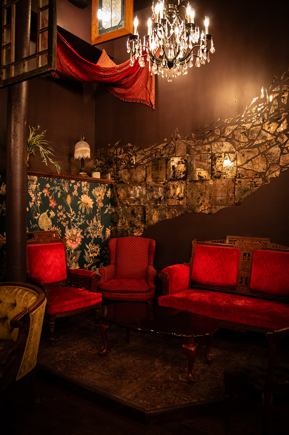 Red velvet couches on a stage backed up against a wall with our chandelier, hanging tapestries and a fragmented mirror art piece
