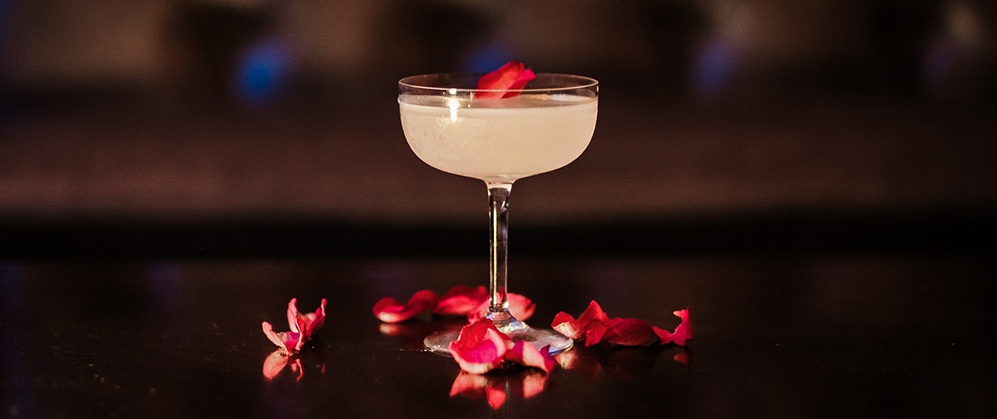 A cocktail in a coupe glass with rose petals