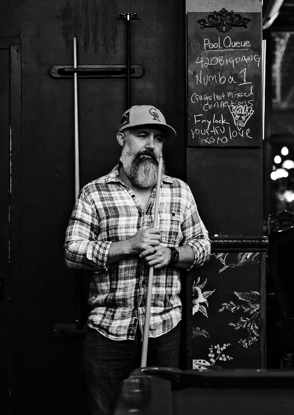 Large bearded customer standing in front of the chalkboard for pool queue