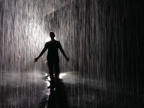 The Rain Room inside a museum in Los Angeles - a man stands amidst rain falling all around him, lit from behind