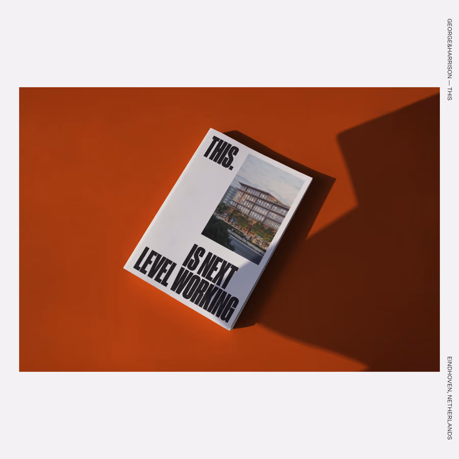 A white booklet with bold black text reading “THIS. IS NEXT LEVEL WORKING” and a rendering of a modern office building on the cover, placed on an orange surface.