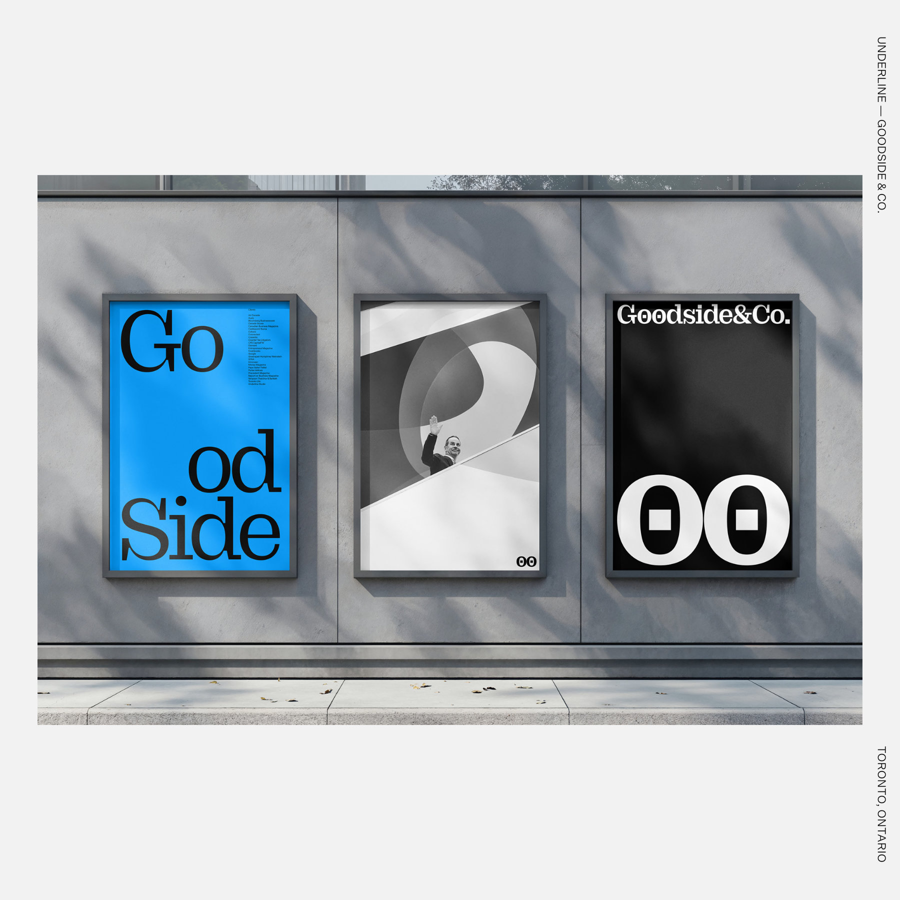 Three framed posters on a concrete wall feature bold black-and-white graphic designs, including “Goodside&Co.” text and a central image of a person waving from behind a curved architectural form.