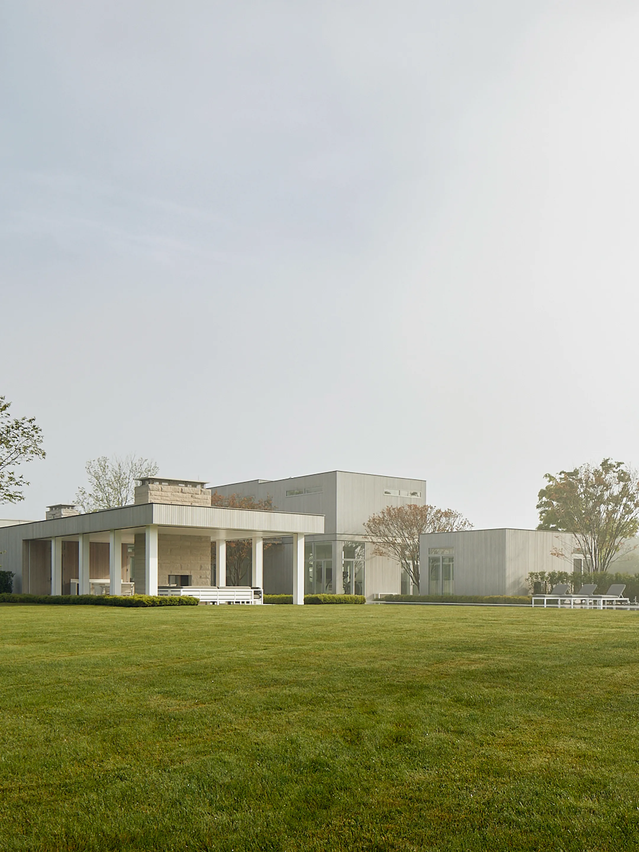 Low modern house with a covered terrace overlooking a broad lawn.